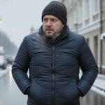 Mężczyzna w czarnej czapce i kurtce spaceruje zimą po miejskiej ulicy】【。